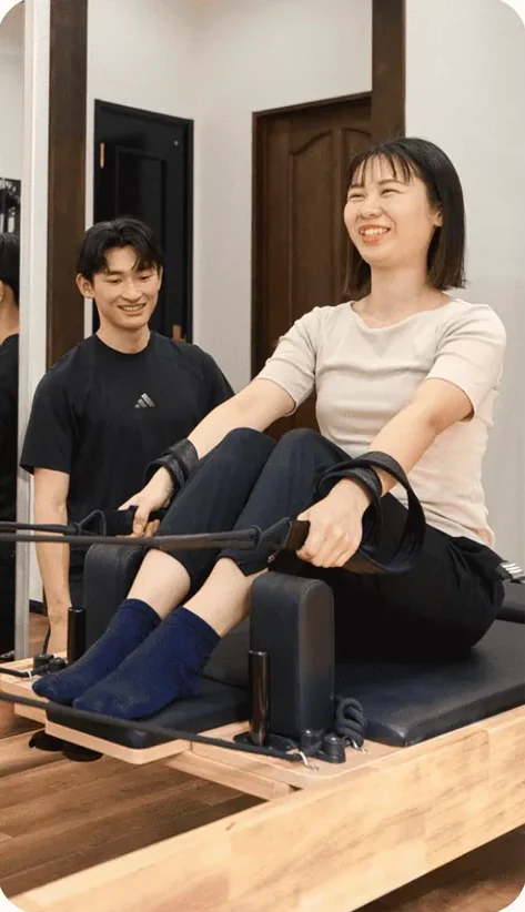 トレーナーの指導でマシンピラティスに取り組み笑顔を見せる女性