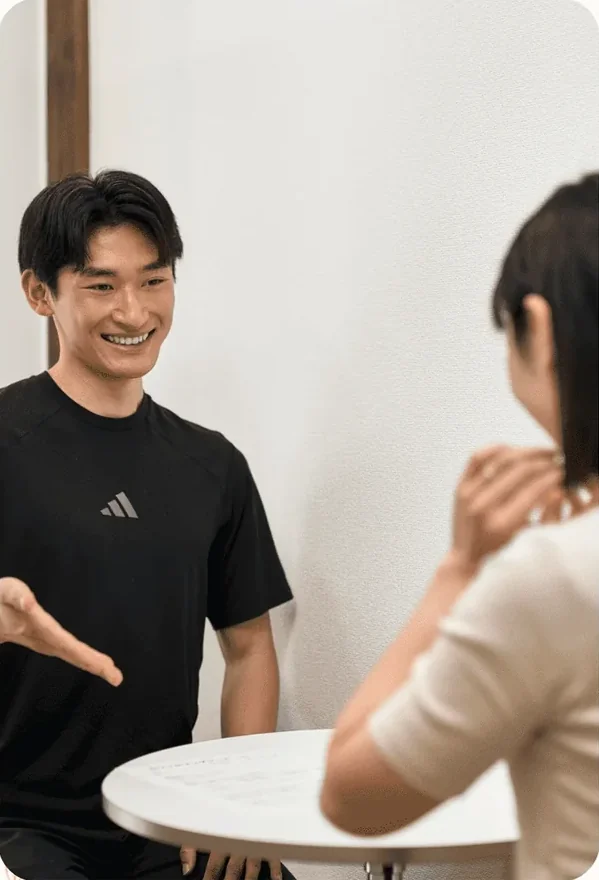 テーブルを挟んで会員と目標や食事について話すトレーナー