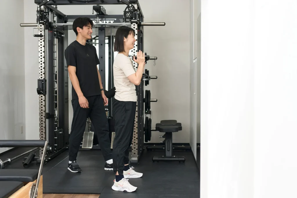 マシンでのトレーニングを指導するトレーナーと女性会員