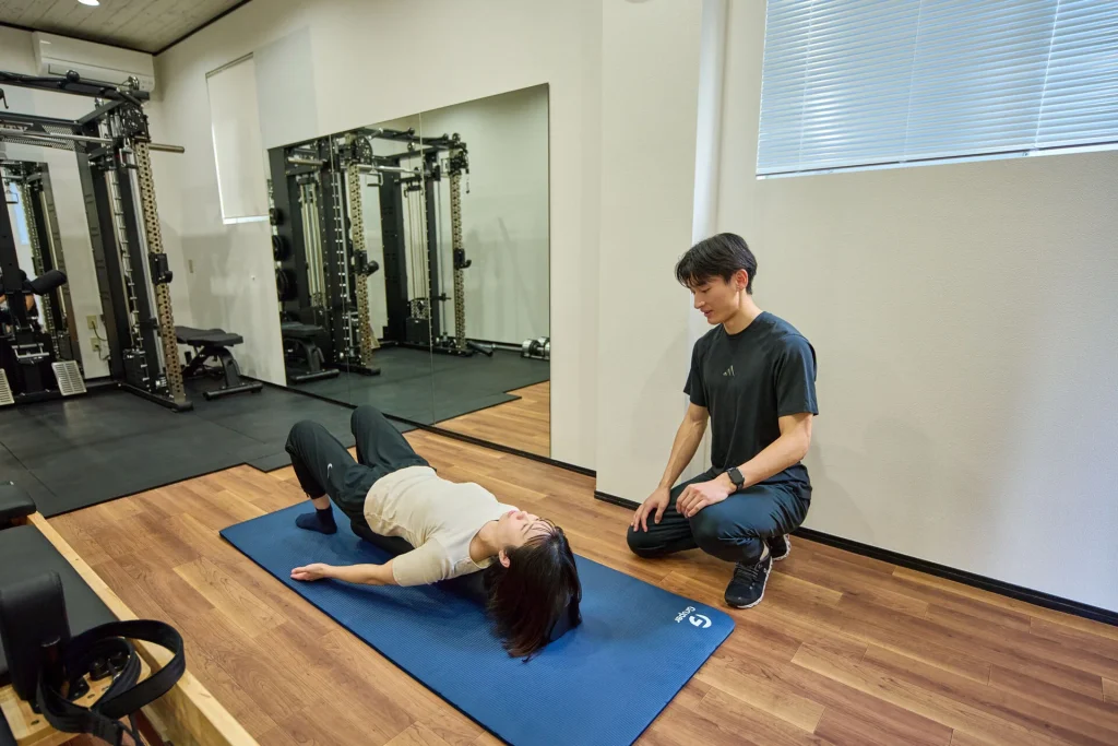 マットでのエクササイズを指導するトレーナーと女性会員