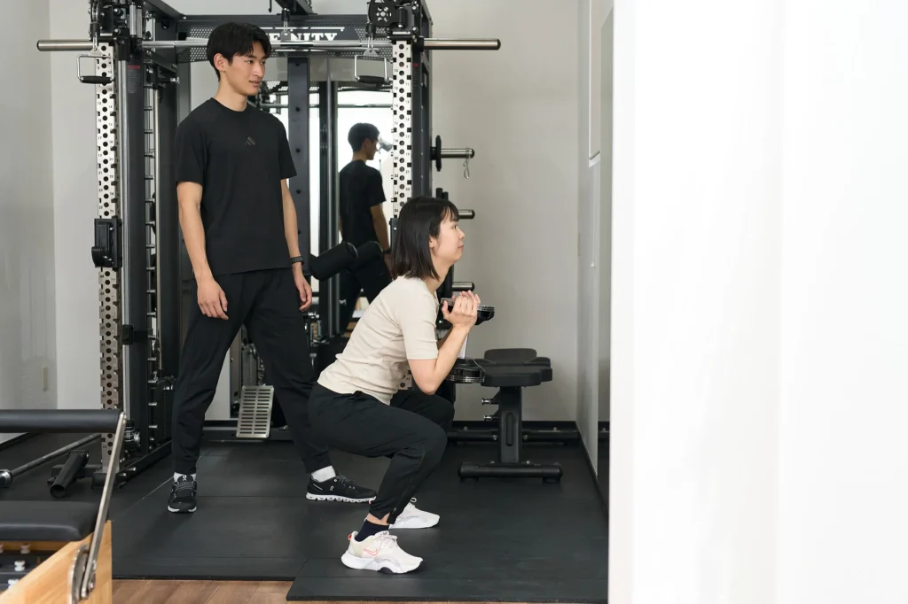 スクワットを指導するトレーナーと女性会員