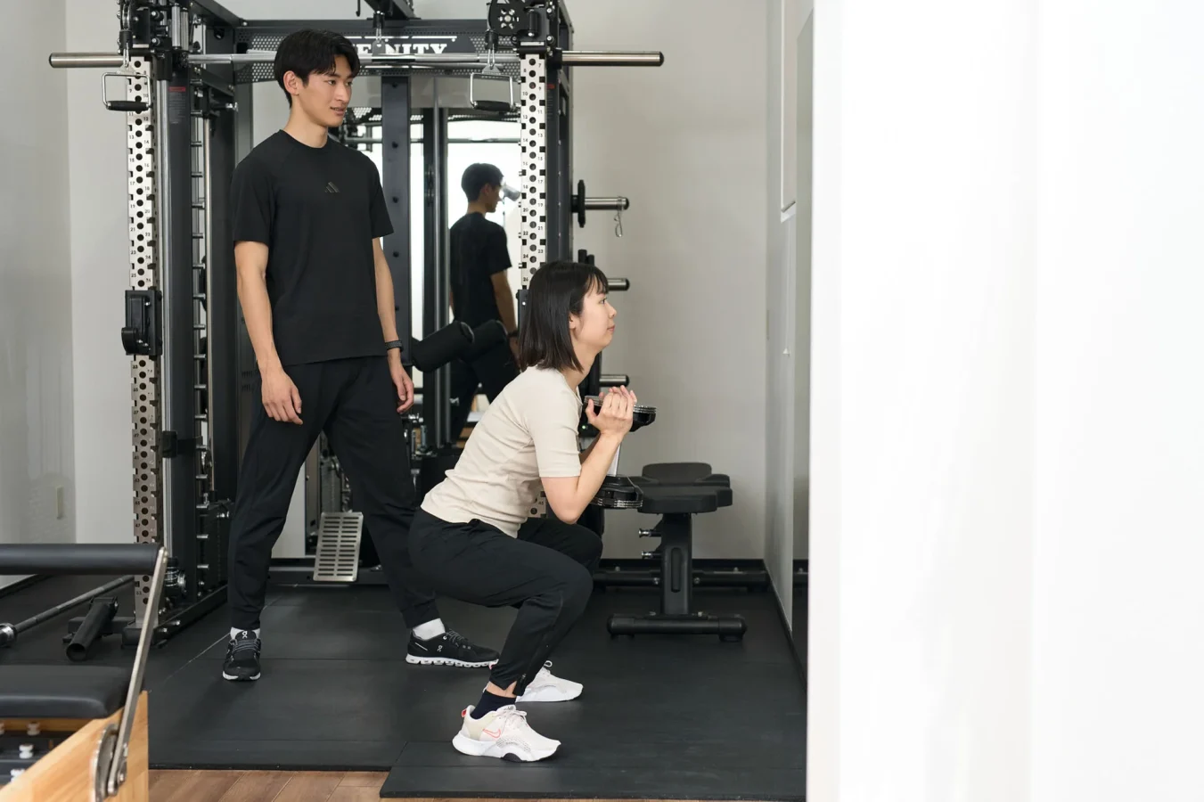 スクワットを指導するトレーナーと女性会員