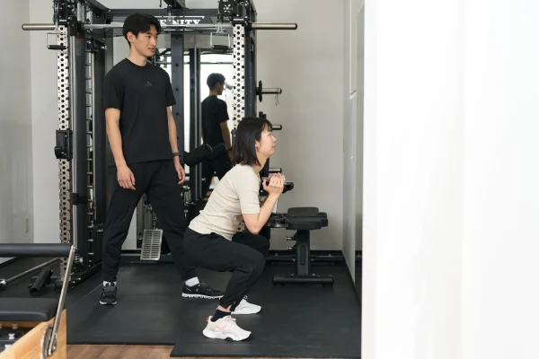 スクワットを指導するトレーナーと女性会員