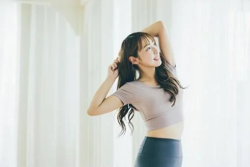 カーテン越しの光の中で伸びをする女性